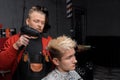 A professional Caucasian barber busy working drying hair dryer guy's client haircut hairdresser