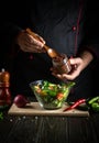 Professional chef adds flavoring to the vegetable salad. Vegetarian food by hands of the cook in the kitchen