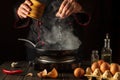 Professional chef adds salt while cooking eggs or an omelet in pan. Work environment on kitchen table. Menu idea for a restaurant Royalty Free Stock Photo