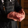 Professional chef in black apron holding large piece of raw meat steak ready for cooking. Uncooked fatty meat fillet in Royalty Free Stock Photo