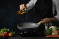 The professional chef in black apron pouring oil into pan wok at restaurant kitchen on dark blue background. Backstage of cooking Royalty Free Stock Photo