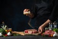 Professional chef in black uniform pours mustard on raw steak on wooden chopped board. Backstage of preparing grilled pork meat at