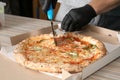 Professional chef cutting Italian oven baked pizza on table