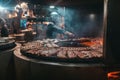 Professional chef grills pork or beef ribs on an open round grill oven in a restaurant