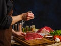 Professional chef prepares juicy steaks from fresh meat on a wooden cutting board, dark background. Sprinkle the pieces of meat