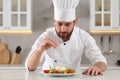 Professional chef salting delicious salad at marble table in kitchen