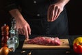 Professional chef sprinkles the raw beef meat with salt. Preparing meat before baking. Working environment in kitchen of Royalty Free Stock Photo