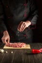 Professional chef sprinkles raw meat with salt. Preparing beef meat before baking. Working environment in the kitchen Royalty Free Stock Photo