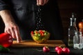 Professional chef sprinkles salt salad of fresh vegetables on wooden table. Preparing healthy food on the kitchen restaurant Royalty Free Stock Photo