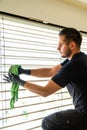 Professional cleaner deep cleaning window blinds in an apartment with a green microfiber cloth Royalty Free Stock Photo