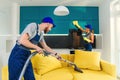 Young man vacuums yellow sofa and cute girl wiping kitchen furniture. Professional cleaners in apartment. Royalty Free Stock Photo