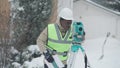 Professional confident geodesist using theodolite outdoors on snowy winter day. Middle shot portrait of serious African