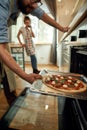 Professional cook making pizza at home. Man putting raw pizza in modern oven for baking. Woman standing in the Royalty Free Stock Photo