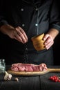 Professional cook prepares raw veal meat. Before baking chef adds salt to the beef. National dish is being prepared in the Royalty Free Stock Photo