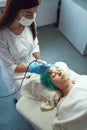 A professional cosmetologist performs an ultrasonic phonophoresis procedure for a young woman.