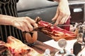 Professional cutter carving slices from a whole bone. Spanish ham