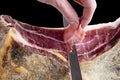 Professional cutter hand carving slices from a whole bone serrano jamon. Knife cutting a spanish serrano ham. Hands of a chef cutt