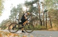 Professional cyclist in sport outfit stands with bicycle on country forest road on background of autumn landscape at sunset. Royalty Free Stock Photo