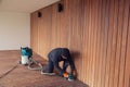 Deck worker kneeling while sanding wooden deck with orbital power sander