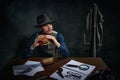 Professional detective in fedora hat sitting at table and eating delicious burger for lunch over dark green vintage Royalty Free Stock Photo