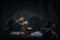 Professional detective in fedora hat sitting at table with thoughtful face and drinking coffee over dark green vintage