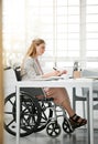 Professional, disabled business woman in wheelchair reading documents, writing or making notes on office desk sitting by Royalty Free Stock Photo