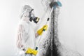 A professional disinfector in overalls processes the walls from mold with a brush. Removal of black fungus in the apartment and ho