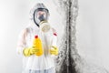 A professional disinfector in overalls and a respirator is holding cleaners in the hands against the background of a white wall, a