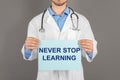 Professional doctor holding sheet of paper with phrase NEVER STOP LEARNING on background, closeup