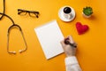 Professional doctor writing medical records in a notebook with stethoscope, coffee cup and heart Royalty Free Stock Photo