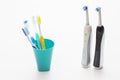 Professional Electric Toothbrushes In Front of Four Manual Tooth Brushes in One Cup On White Background