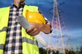 Electrician with drafting and helmet near high voltage tower, closeup