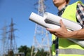 Professional electrician with draftings near high voltage tower, closeup