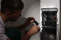 Professional electrician with flashlight fixing refrigerator