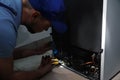 Professional electrician with flashlight fixing refrigerator