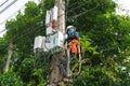 A professional electrician performs installation work on a pole. An electrician in professional equipment, working in dangerous