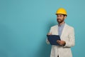 Professional engineer in hard hat with clipboard on light blue background, space for text Royalty Free Stock Photo