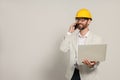 Professional engineer in hard hat with laptop talking on phone against white background, space for text Royalty Free Stock Photo