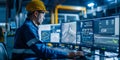 The professional engineer in a hard hat is working on the computer with multiple monitors in a large industrial plant control room Royalty Free Stock Photo