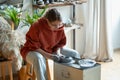 Professional enthusiastic woman artificer works sits near potters wheel making jugs from clay