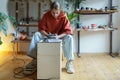 Professional enthusiastic woman artificer works sits near potters wheel making jugs from clay