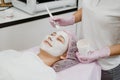 Professional Esthetician Apply Face Mask to the client`s face in spa beauty center. Young woman getting facial care by beautician