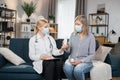 Professional family gp doctor in mask consulting elderly 60 aged woman patient at home. Female nurse showing a new oral Royalty Free Stock Photo