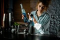 Professional female bartender pours blue drink from jigger into cup.