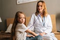 Professional female doctor listening to heartbeat with stethoscope to check up little sick girl sitting in bed at home. Royalty Free Stock Photo