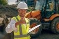 Female construction worker in protective helmet standing against a tractor on construction site Royalty Free Stock Photo