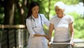 Professional female nurse supporting old woman moving in park with walking frame