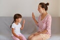 Professional female physiotherapist working on speech defects or difficulties with small child girl indoors while sitting on sofa Royalty Free Stock Photo