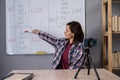 Professional female teacher explaining new theme to students, having video call, sitting near whiteboard with grammar Royalty Free Stock Photo