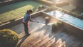 professional female worker cleaning terrace with a power washer - high water pressure cleaner on wooden terrace surface